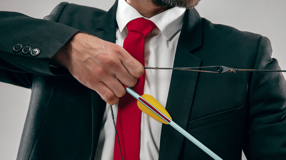Businessman aiming at target with bow and arrow isolated on gray studio background. The business, goal, challenge, competition, achievement, purpose, victory, win, clarity, winner and success concept