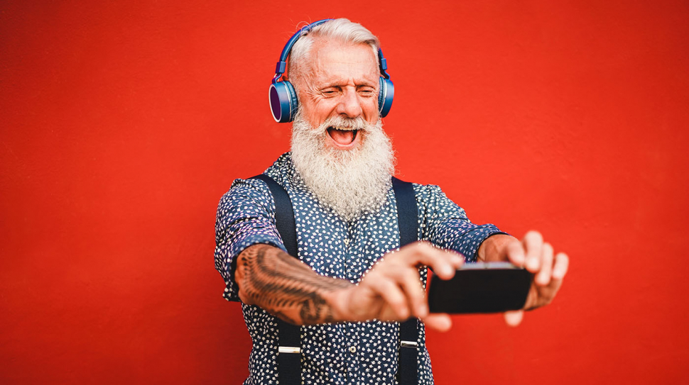 Senior hipster man using smartphone app for creating playlist with rock music - Trendy tattoo guy having fun with mobile phone technology - Tech and joyful elderly lifestyle concept - Focus on face